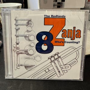 Pode incluir: Uma caixa de CD com fundo branco e um desenho de uma trombeta. O título do CD é "The Redlands 8-ja Who's Counting?"
