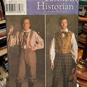 May include: A vintage sewing pattern titled "The Fashion Historian" by Martha McCain. The pattern features illustrations of historical men's clothing, including trousers, vests, and shirts. The cover has a purple and white banner with the title.