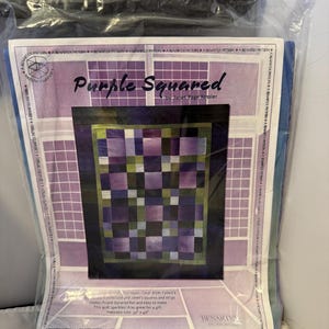 May include: A Benartex pattern titled "Purple Squared" by Janet Page Kessler. The pattern features a quilt design with squares in shades of purple, green, and blue. The finished size is 32" x 40". The pattern is packaged in a clear plastic bag.