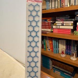 May include: A clear plastic package containing a patchwork border stencil. The stencil features a repeating pattern of blue hexagons with dashed lines, and the text "Embossalicious" is visible at the top.