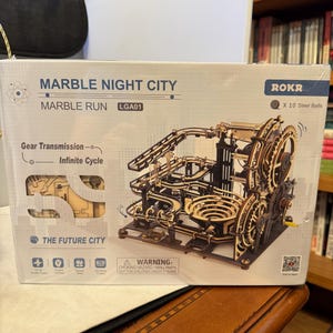 May include: A wooden Marble Night City marble run kit. The box features the text "Marble Night City" and "Marble Run". The kit includes 10 steel balls and has a gear transmission for an infinite cycle. The Future City is also printed on the box.