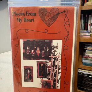 Könnte beinhalten: Ein Bastelmuster mit dem Titel "Pieces From My Heart" in einer durchsichtigen Plastiktüte. Das Cover ist rot mit einem Herzdesign und dem Text "Pieces From My Heart" und "I Believe #132". Das Muster zeigt Illustrationen von Volkskunstfiguren.
