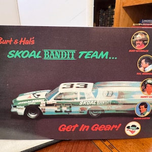 Op de afbeelding: Een zwart-witte promotieposter voor het Skoal Bandit Team. De poster toont een groene en witte raceauto met nummer 33 aan de zijkant. De poster toont ook vier foto's van de teamleden, waaronder Burt Reynolds, Hal Needham, Harry Gant en Travis Carter. De tekst op de poster luidt "Burt & Hal's Skoal Bandit Team... Get In Gear!"