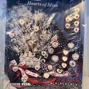Puede incluir: Un folleto para un folleto de patrones de punto de cruz titulado "This and That Hearts of Mine" de Yvonne M. Thorp. El folleto es de Spinning Wheel y cuesta $3,95. La portada presenta una variedad de diseños de corazones de punto de cruz.