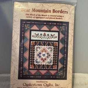 May include: A quilt pattern for a quilt block called "Bear Mountain Borders". The pattern features a variety of appliqued and pieced borders. The pattern is distributed by Quakertown Quilts, Inc. and includes the company's address, phone number, and fax number.