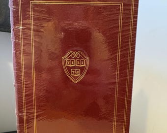 May include: A burgundy leather-bound book with gold accents and a gold embossed Harvard University seal on the front cover. The book is wrapped in plastic.