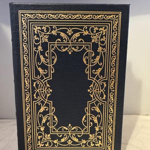 May include: A dark blue leather-bound book with a gold-colored decorative border.