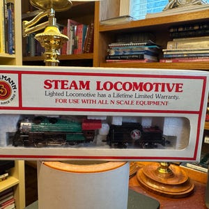 May include: A boxed Bachmann Steam Locomotive model. The box is white with red text that reads "STEAM LOCOMOTIVE". The model train is green and black. The box also includes the text "FOR USE WITH ALL N SCALE EQUIPMENT".