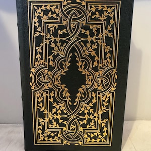 May include: A black leather-bound book with a gold-leaf design of intricate vines and swirls on the cover.