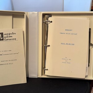 May include: An open, off-white binder with printed papers inside. The papers include the text "WORDSCOPE Computer Action Learning" and "CAL computer action learning". A black pen is visible.