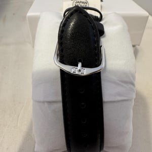 May include: Black leather watch band with a silver buckle. The band is in a white box with the text "JAPAN MOV'T" on a label.