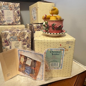 May include: A collection of "Cherished Teddies" figurines and boxes. A teddy bear figurine sits in a pink teacup with a candy cane. Boxes feature teddy bear illustrations and the "Cherished Teddies" logo.