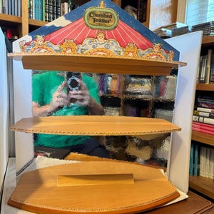 Może przedstawiać: Drewniana półka ekspozycyjna z trzema poziomami. Górna część posiada ozdobny nagłówek z napisem "Cherished Teddies". Półki wykonane są z jasnego drewna z falistą krawędzią.