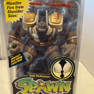 Puede incluir: Figura de acción Ultra-Action Deluxe Edition de Badrock de la serie de cómics Spawn de Todd McFarlane. La figura de acción es azul, dorada y marrón, con misiles que se disparan desde silos en los hombros. El embalaje incluye el texto "America's Best Selling Comic Book."