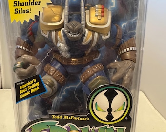 May include: Deluxe Edition Ultra-Action Figure of Badrock from Todd McFarlane's Spawn comic book series. The action figure is blue, gold, and brown, with missiles that fire from shoulder silos. The packaging includes the text "America's Best Selling Comic Book."