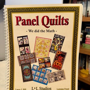 May include: A spiral-bound book titled "Panel Quilts" with the subtitle "- We did the Math -". The cover has a gold border and displays various quilt panel designs. Authors are Lacey J. Hill and Lorraine Freed, published by L&L Studios.