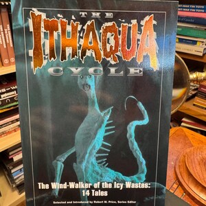 Puede incluir: Un libro de bolsillo titulado The Ithaqua Cycle: The Wind-Walker of the Icy Wastes: 14 Tales. La portada presenta un fondo azul oscuro con una ilustración central de una criatura esquelética pálida y letras metálicas naranjas para el título.