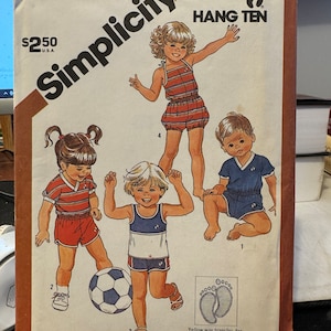 Op de afbeelding: Simplicity naaipatroon nummer 5953 voor Hang Ten kleertjes voor peuters. Het patroon bevat instructies voor drie verschillende outfits: een rood-wit gestreepte jumpsuit, een rood-wit gestreept shirt met rode shorts en een blauw-wit gestreept shirt met blauwe shorts. Het patroon is geschikt voor stretch-breistoffen en bevat Time-Saver stretch-breimethoden.