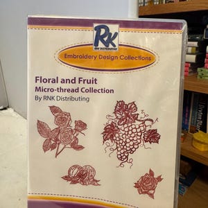 Può includere: Una confezione sigillata per una collezione di disegni per ricamo. La copertina presenta il testo "Floral and Fruit Micro-thread Collection" e illustrazioni di rose, uva e altri elementi floreali. Il logo del marchio "RK" è in alto.