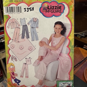 Puede incluir: Un sobre de patrón de costura Simplicity para ropa de estar por casa de Lizzie McGuire, que incluye una camiseta sin mangas, pantalones y una manta. El paquete muestra ilustraciones de variantes, un modelo en rosa y el texto Lizzie McGuire.