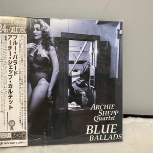 Könnte beinhalten: Ein CD-Cover für "Blue Ballads" von Archie Shepp Quartet. Das Cover zeigt ein Schwarz-Weiß-Bild einer Frau und eines Mannes mit Hut. Der Text auf dem Cover enthält den Namen des Künstlers und den Albumtitel sowie japanischen Text.