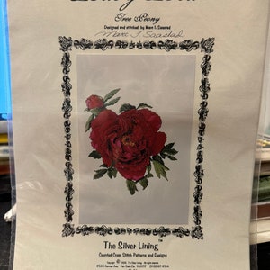 Puede incluir: Un patrón de punto de cruz titulado "Ruby Red" con una imagen detallada de una flor de peonía roja con hojas verdes. El diseño es de Mare I. Saastad y forma parte de los patrones de punto de cruz contados "The Silver Lining".