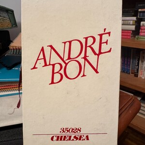 May include: A rectangular, off-white box with the words "ANDRÉ BON" in large, red, stylized font. Below, smaller red text reads "35028 CHELSEA". The box is likely packaging for a product.