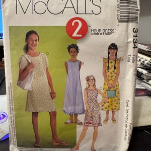 May include: McCall's sewing pattern for a girl's dress. The pattern is called "Hour Dress" and is size 12-14-15. The pattern includes three different styles of dresses, all with a floral print.