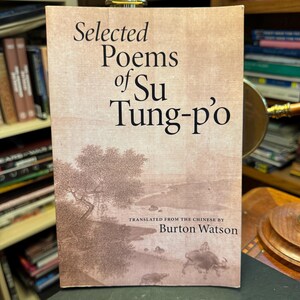 Op de afbeelding: Een paperbackboek getiteld Selected Poems of Su Tung-p'o, vertaald door Burton Watson. De kaft bevat een sepia-kleurige landschapsillustratie met een boom, een rivier en een figuur op een waterbuffel, tegen een lichte achtergrond.