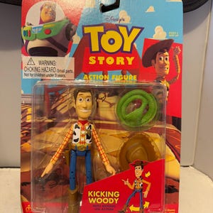 May include: A Toy Story "Kicking Woody" action figure in its original packaging. The packaging features Woody, a green snake, and a cowboy hat. The text on the packaging reads "Toy Story Action Figure" and "Kicking Woody with Kicking Leg Action".
