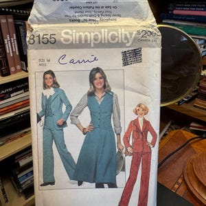 Può includere: Una busta per cartamodello Simplicity, numero 8155, taglia 14, con illustrazioni di tre completi: un set giacca e pantaloni blu, un completo gilet e gonna blu con camicia a righe e un tailleur giacca e pantaloni color ruggine.