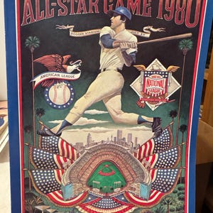 May include: A vintage 1980 All-Star Game program featuring a baseball player in a blue cap and white uniform, swinging a bat. The program features a backdrop of Dodger Stadium with American flags and a price of $2.50.