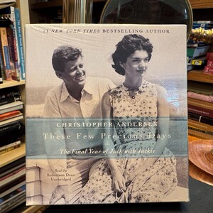 May include: A square-shaped audiobook box set titled These Few Precious Days: The Final Year of Jack with Jackie by Christopher Andersen. The cover features a black and white photograph of John F. Kennedy and Jacqueline Kennedy sitting together.