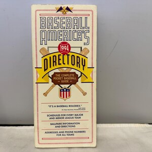 Op de afbeelding: Een vintage "Baseball America's Directory" uit 1994. De cover toont de titel in vette, gestileerde letters, met een honkbal- en knuppelafbeelding. De gids bevat schema's, stadioninformatie en teamcontactgegevens. De cover is crèmekleurig met rode en gele accenten.