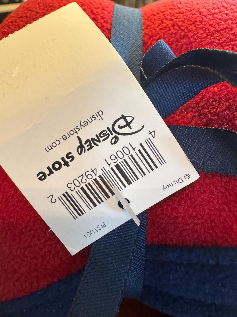 K&ouml;nnte beinhalten: Eine rote Decke mit blauen Zierleisten und einem blauen Band. Ein wei&szlig;es Etikett mit dem Disney Store-Logo und Barcode ist an der Decke befestigt. Das Etikett enth&auml;lt auch den Text "disneystore.com".