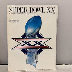 Può includere: La copertina del programma del Super Bowl XX presenta un trofeo di football blu. Il programma elenca i Chicago Bears contro i New England Patriots. Il testo "SUPER BOWL XX" è in alto.