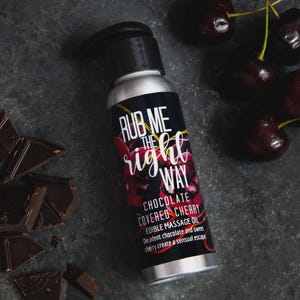 May include: A silver bottle of "Rub Me The Right Way" chocolate covered cherry edible massage oil. The label features the text in white and red, with cherries and chocolate pieces scattered around.