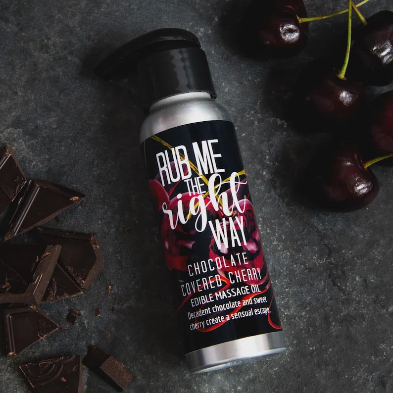 May include: A silver bottle of "Rub Me The Right Way" chocolate covered cherry edible massage oil. The label features the text in white and red, with cherries and chocolate pieces scattered around.