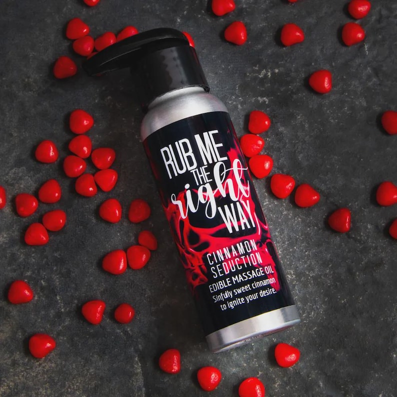 Our edible massage oil "Cinnamon Seduction" is shown surrounded by red hot candies on a dark stone background. This lickable massage oil is packaged in a lightweight aluminum bottle with a convenient pump top.