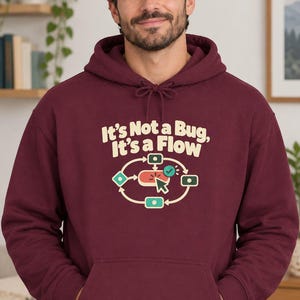May include: A maroon hooded sweatshirt featuring a graphic print with the text "It's Not a Bug, It's a Flow" above a circular diagram of interconnected icons, including a computer mouse cursor, a checkmark, and various square shapes.