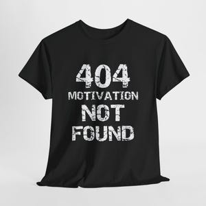 Könnte beinhalten: Schwarzes T-Shirt mit dem Text "404 Motivation Not Found" in weißer, verwaschener Schrift. Das Shirt hat einen Rundhalsausschnitt und kurze Ärmel, geeignet für Freizeitkleidung.