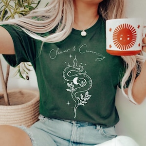 Könnte beinhalten: Ein dunkelgrünes T-Shirt mit einem weißen Schlangenmotiv und dem Text "Clever & Cunning".
