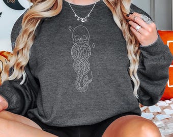 May include: A dark gray sweatshirt with a white outline of a snake with a skull at the top. The snake is coiled and has a diamond shape at the top and bottom. The sweatshirt has a relaxed fit.