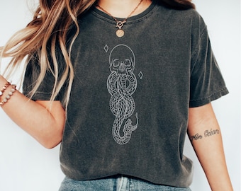 May include: A dark gray t-shirt with a white outline of a snake with a skull at the top. The snake is in the shape of the Hogwarts house symbol for Slytherin.