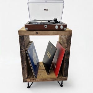 May include: A wooden record player stand with a brown turntable and a clear plastic cover. The stand has a rustic, reclaimed wood appearance and holds vinyl records. The stand has black metal legs and is set against a white background.