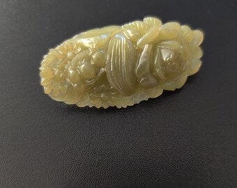 May include: A green jade carving of a flower with leaves and buds. The carving is detailed and intricate.