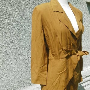 May include: A mustard yellow suit with a long-sleeved jacket and a skirt. The jacket has a wrap-style closure and a bow at the waist.