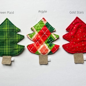 May include: Three Christmas tree-shaped coasters with different patterns. The first coaster is green plaid, the second is red and green argyle, and the third is red with gold stars.