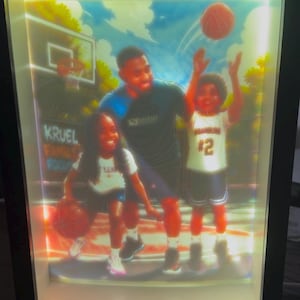 May include: A rectangular, illuminated shadow box frame containing a colourful illustration of an adult and two children playing basketball on an outdoor court. The scene features a basketball hoop, a basketball in motion, and the text KRUEL FAMILY.