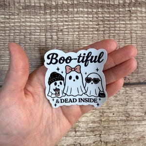 May include: A white sticker with the text "Boo-tiful & DEAD INSIDE" and illustrations of three ghosts. One ghost wears a beanie and holds a coffee cup, another wears a bow, and the third wears sunglasses.